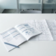 Opengeslagen vereistendocument en architectonische plattegrond op wit bureau met blauwe pen, minimalistische kantooromgeving.